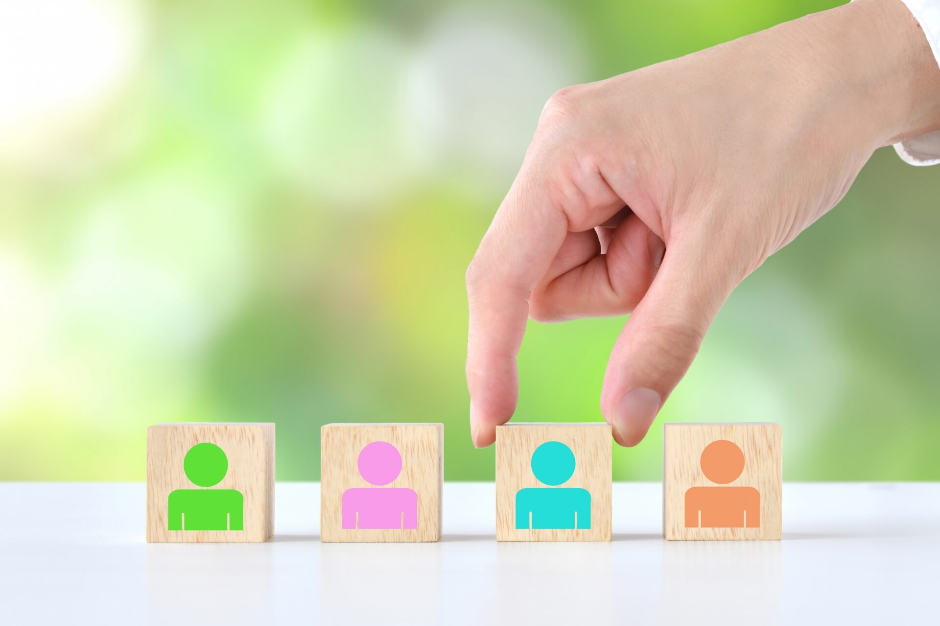人材の選定や配置を表すイメージ（人物アイコンのブロックを手で選ぶ様子）