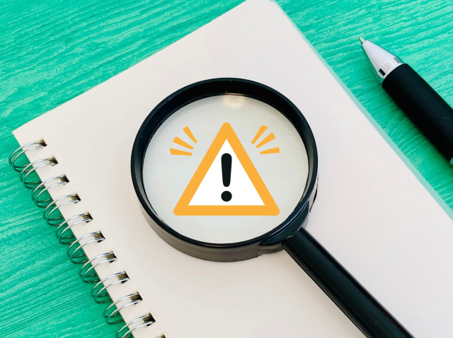 注意マークが書かれた虫眼鏡とノート