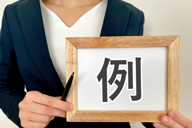 例と書かれたボードを持つ女性の上半身